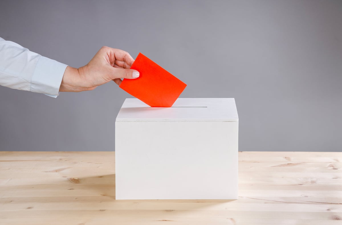 Woman's hand casting a vote and a ballot box. Vote on gray background
