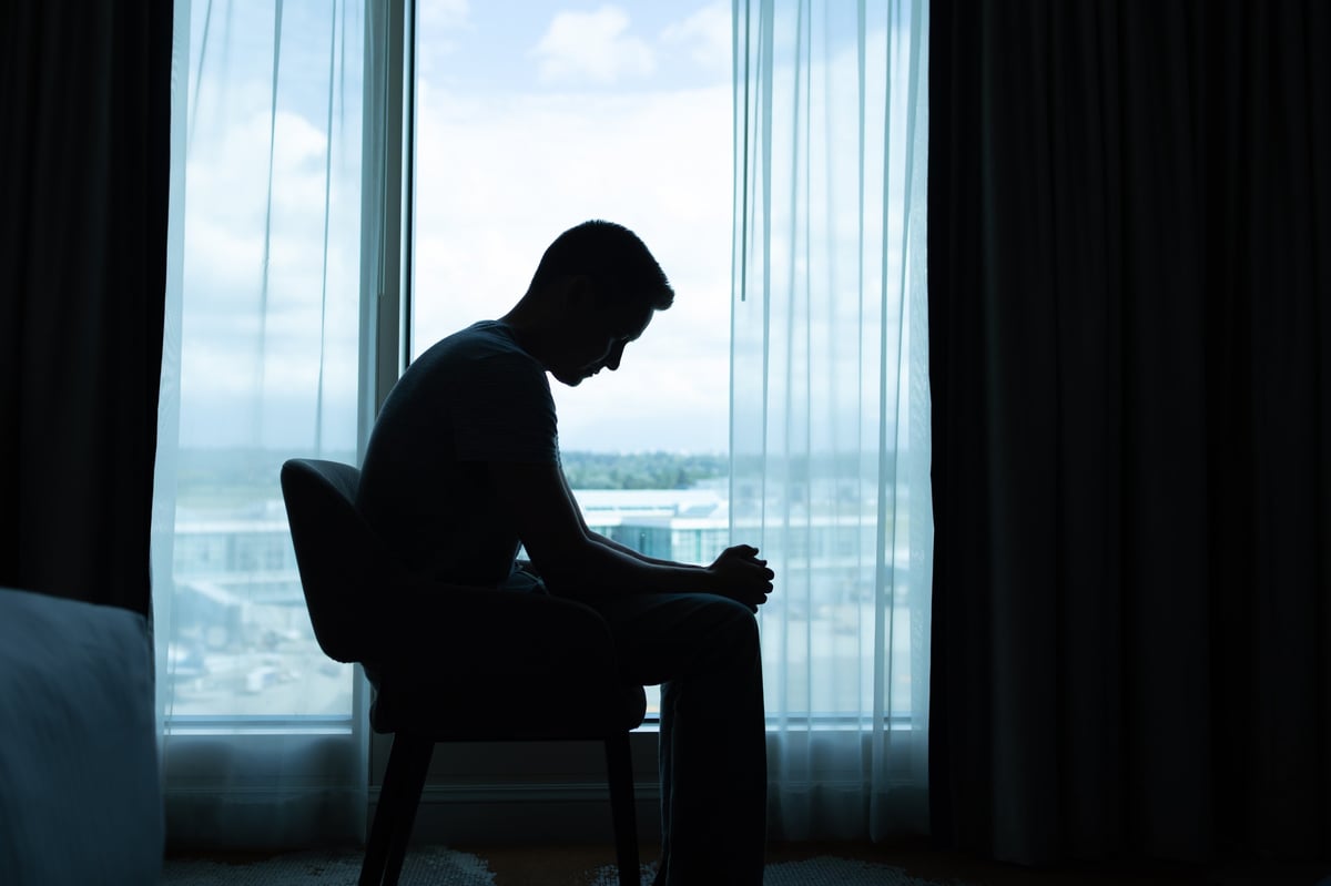 Lonely and sad man sitting in the dark room by himself.
