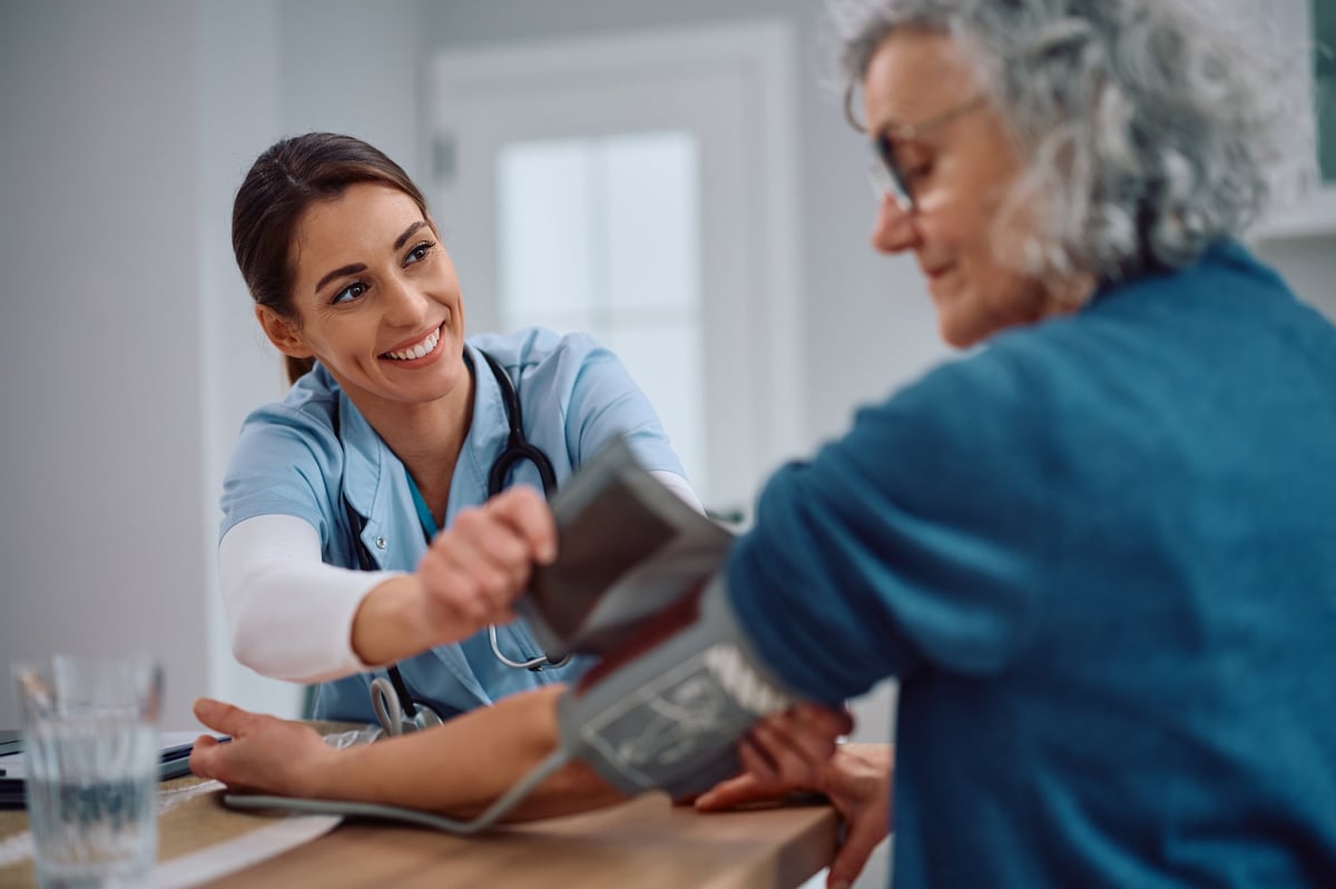 Happy visiting nurse checking blood pressure of a senior woman at home