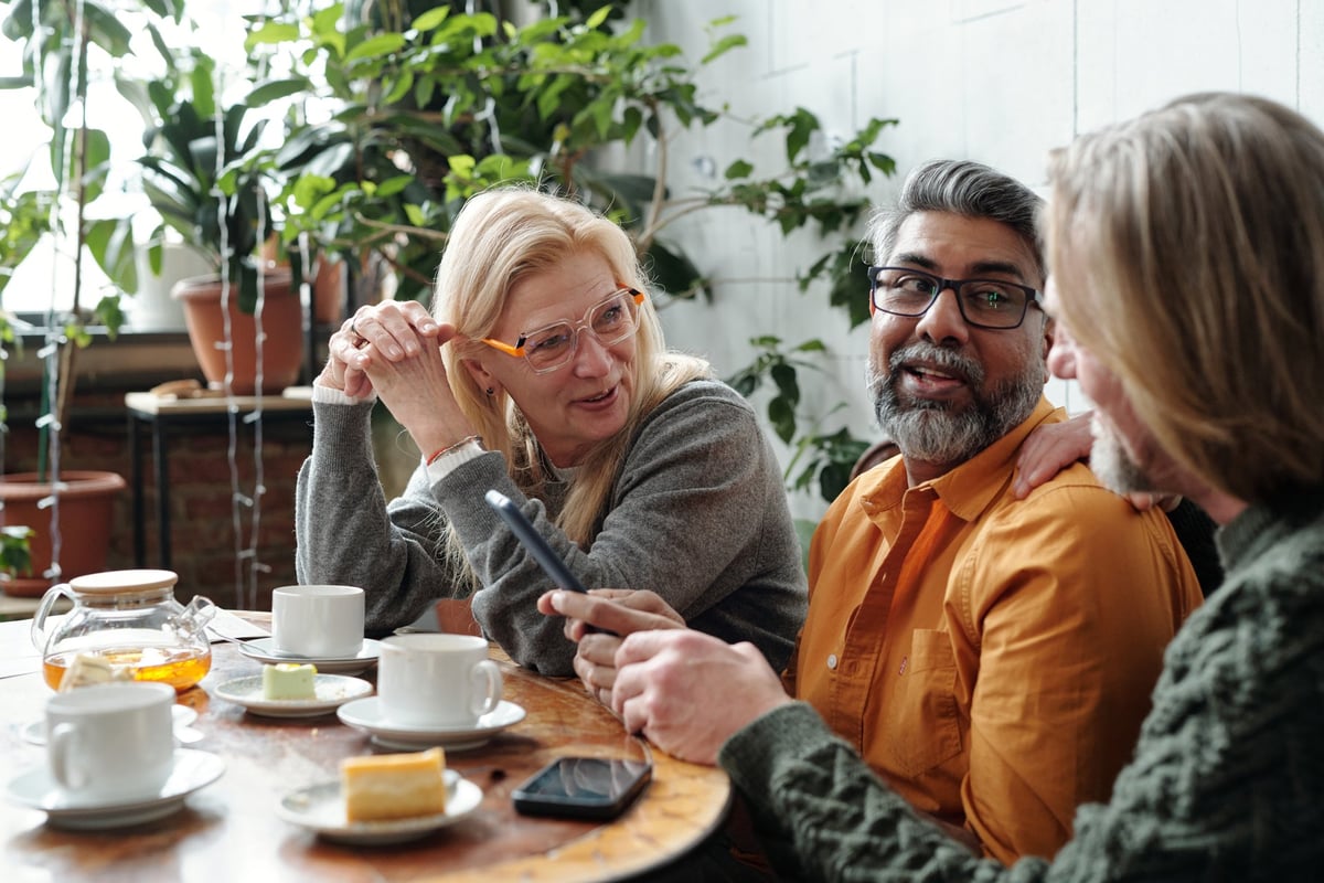 Group of mature friends gathering in cozy cafe, enjoying coffee and pastries while discussing ideas in a relaxed atmosphere