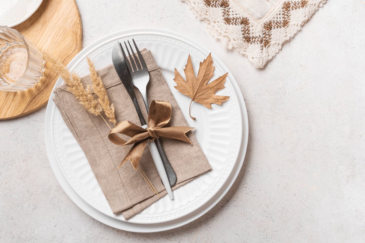 Autumn elegant place setting with dry maple leaves and linen napkins on white background, top view, copy space. White autumn boho style Thanksgiving table setting design.