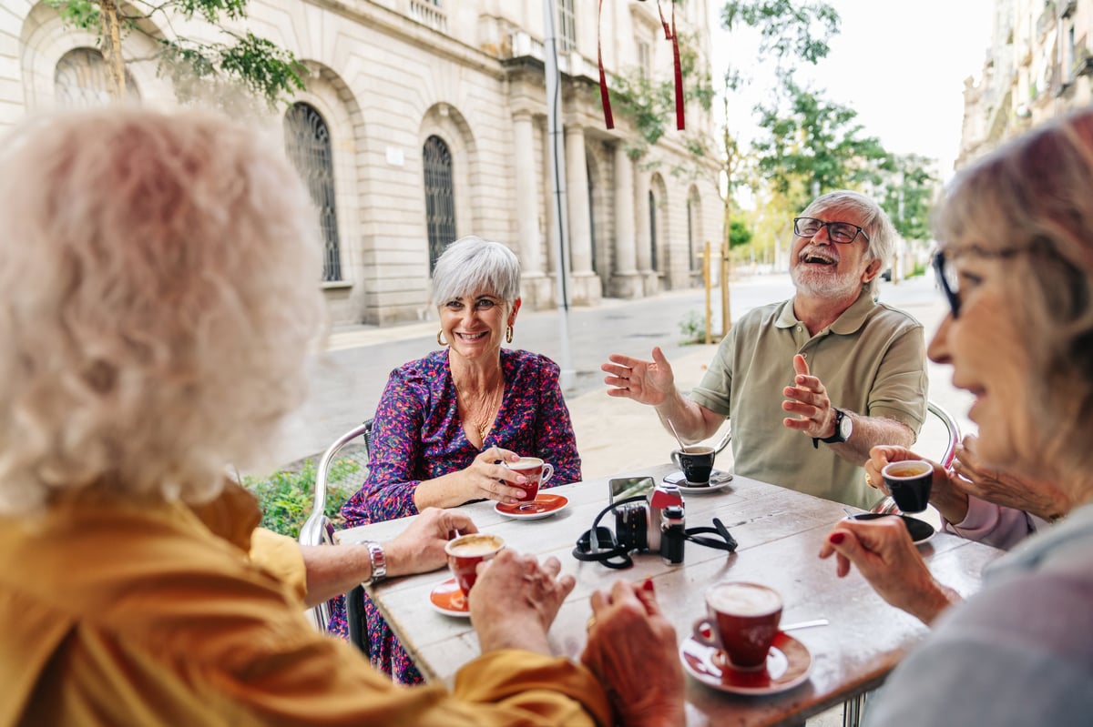 Group of happy senior friends laughing and talking while drinking coffee at a table on a city street cafe terrace