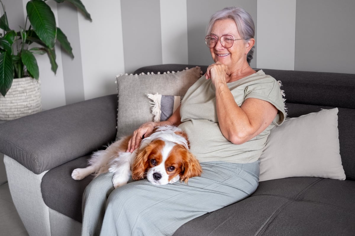 Smiling senior woman sitting on sofa with her dog, comfortable and capable in her home