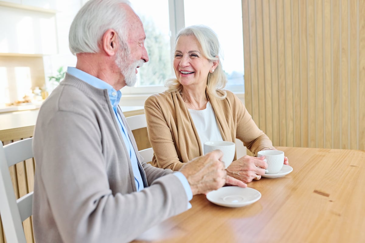 Portrait of a happy senior couple embracing talking and drinking coffee or tea at home