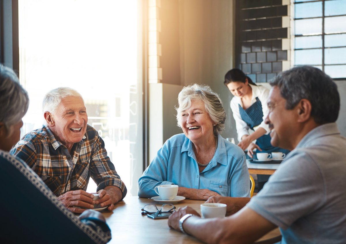 Senior adults sharing a warm, laughing conversation together at a cafe table